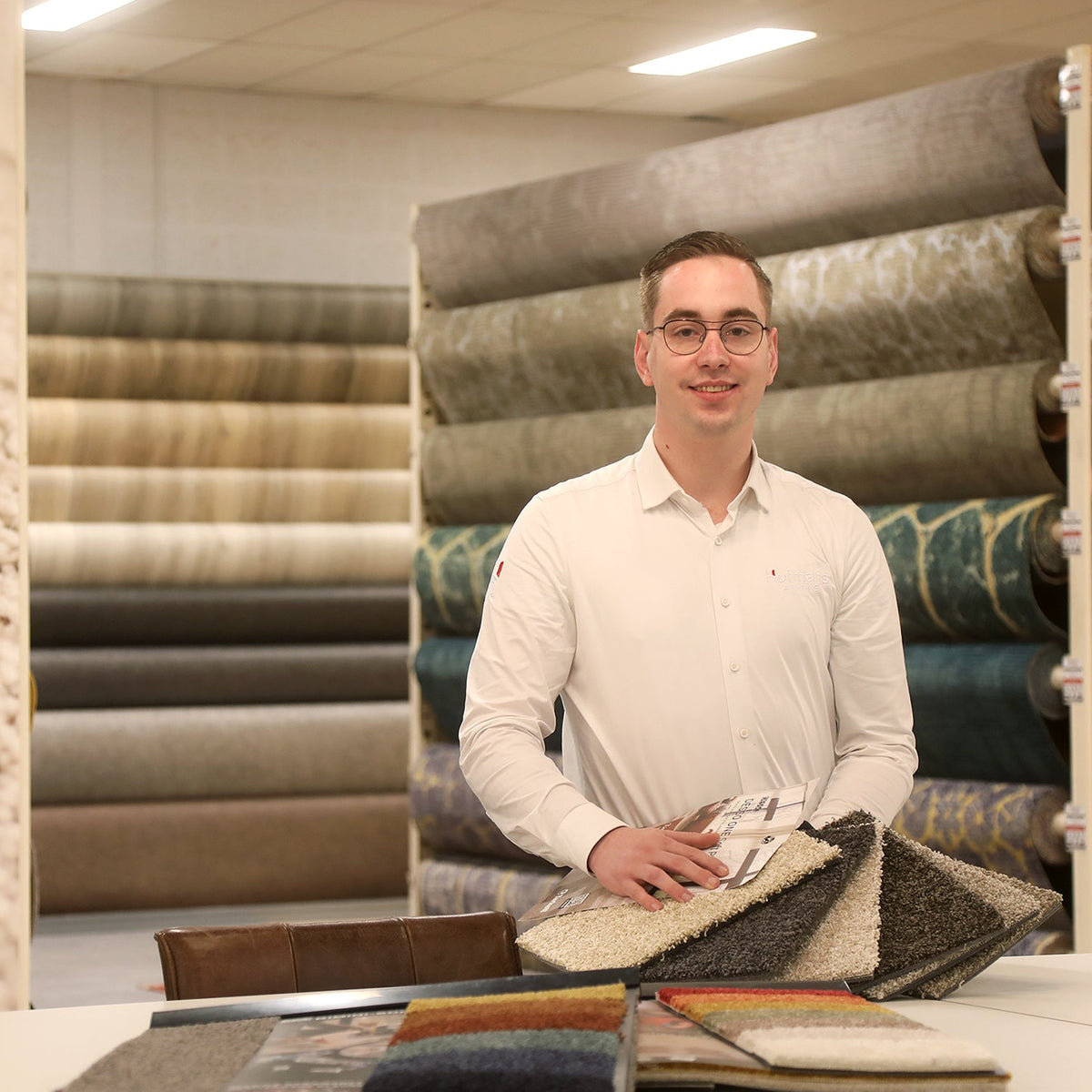 Adviseur Robert in de showroom van Hofmans at Home met diverse kamerbrede rollen tapijt en vloerbedekking in verschillende kleuren en structuren.