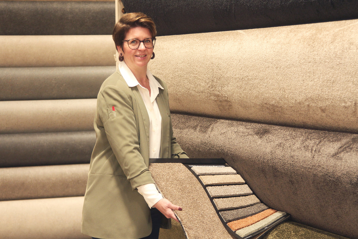 Showroom Hofmans at Home in Cuijk met adviseur Natasja die kamerbrede tapijtstalen presenteert in de vloerenafdeling, onderdeel van de grootste showroom van Nederland.