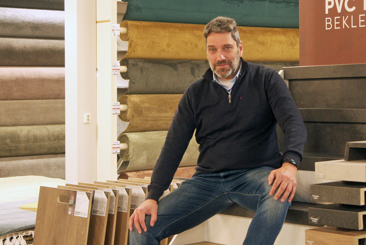Adviseur Rob van Hofmans at Home toont voorbeelden van trapbekleding in PVC en tapijt, omringd door vloer- en tapijtstalen in de showroom.