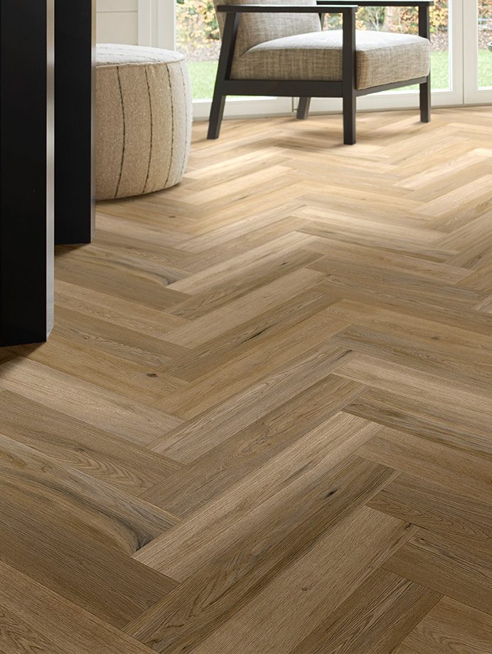 Visgraat PVC-vloer in een lichte houttint in een moderne woonkamer met een fauteuil en poef.