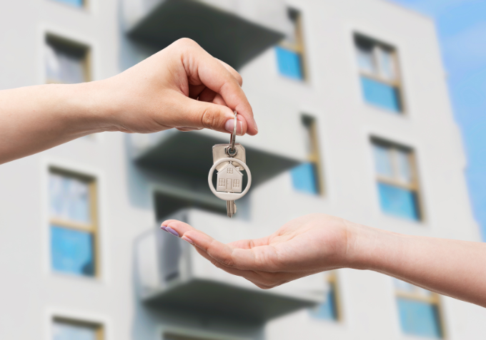Hand geeft een huissleutel aan een andere hand voor een appartementengebouw